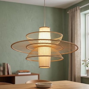 Puede incluir: Una moderna lámpara colgante con un diseño en capas y calado. La lámpara tiene una serie de pantallas circulares concéntricas hechas de finas tiras de madera de tono natural. La fuente de luz es una pantalla cilíndrica de color blanquecino.