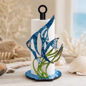May include: A vertical paper towel holder featuring a decorative cutout of a blue angelfish swimming among green seaweed. The base is circular with a blue water-like pattern, and the top has a black metal ring handle for easy carrying.