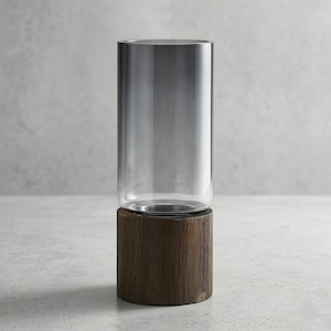 May include: A clear glass cylinder vase with a gradient gray tint, set atop a dark brown, cylindrical wooden base. The vase is a simple, modern design, suitable for displaying flowers or as a decorative piece. The vase is approximately 10 inches tall.