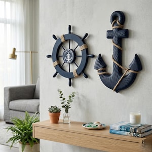 Puede incluir: Decoración mural náutica azul marino con un timón y un ancla. El timón tiene detalles de cuerda y un emblema central. El ancla también es azul marino con detalles de cuerda. La decoración está montada en una pared gris claro.