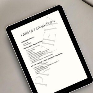 May include: A digital tablet showing a Lash Lift Intake Form. The form includes sections for emergency contact, medical and eye health history, and current medication use. The tablet is black with a white screen, and the text is in a serif font.