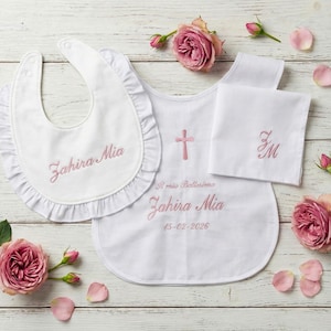 Può includere: Un set battesimo bianco per neonati, composto da bavaglino, top a forma di bavaglino e fazzoletto, tutti ricamati con testo rosa e una croce rosa. Il bavaglino ha un bordo a balze e la scritta "Zahira Mia". Il top riporta la scritta "Il mio Battesimo Zahira Mia 15-02-2026".