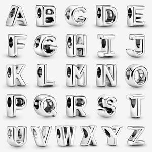 May include: A collection of twenty-six individual silver-toned metal alphabet letter charms, each featuring a smooth, polished finish and a central hole for threading onto a bracelet or necklace chain, arranged in a grid from A to Z.