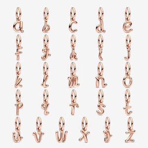 Op de afbeelding: Een verzameling roségouden alfabetbedels, elk in een kleine letterscript. Elke bedel heeft een kleine, heldere edelsteen accent. De bedels zijn ontworpen om te worden gebruikt als hangers of toevoegingen aan armbanden.