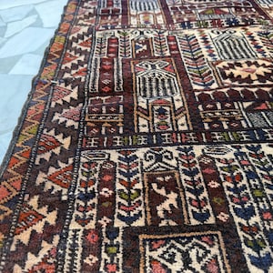 May include: A rectangular area rug featuring a complex geometric pattern with repeating architectural motifs in shades of deep burgundy, cream, navy blue, and muted orange. The design includes intricate borders and stylized floral elements.
