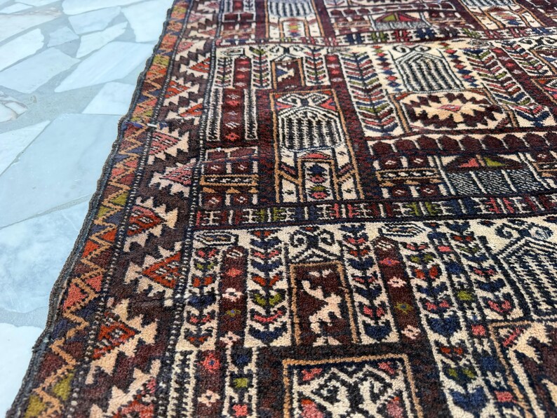 May include: A rectangular area rug featuring a complex geometric pattern with repeating architectural motifs in shades of deep burgundy, cream, navy blue, and muted orange. The design includes intricate borders and stylized floral elements.