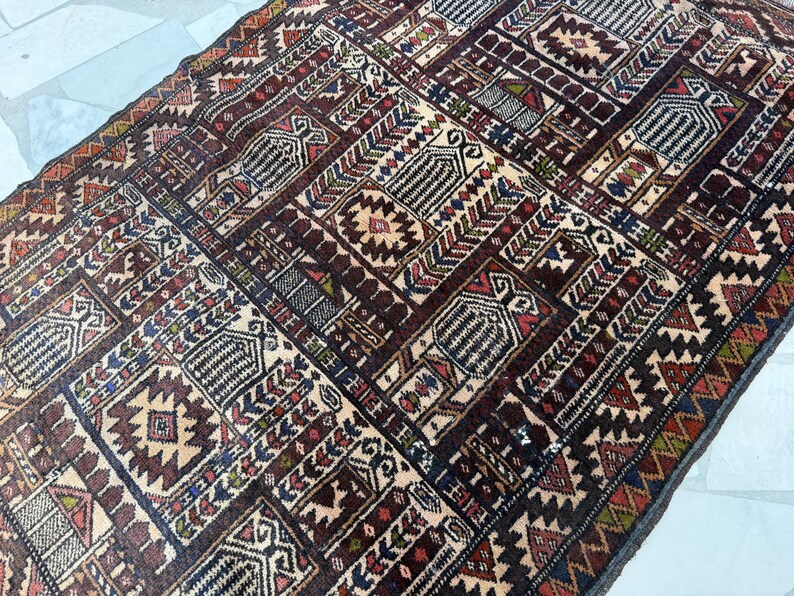 May include: A rectangular area rug featuring a dense, repeating geometric pattern in shades of deep brown, cream, red, blue, and green. The design consists of interconnected rectangular panels containing stylized motifs, serrated borders, and intricate linework.