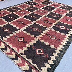 K&ouml;nnte beinhalten: Ein rechteckiger Webteppich mit einem sich wiederholenden geometrischen Muster aus dunkelanthrazitfarbenen, dunkelroten und cremefarbenen Rauten. Das Design umfasst Zickzack-Bord&uuml;ren und kleine Rautenmotive mit pfeilartigen Akzenten.