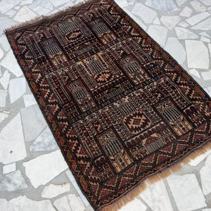 May include: A rectangular woven rug featuring a dark brown, black, and tan geometric pattern with repeating arch motifs and intricate borders. The rug has a short fringe on the top and bottom edges and a dense, symmetrical design throughout.