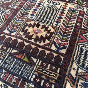 May include: A woven rug featuring a dense, repeating geometric pattern in shades of deep red, navy blue, cream, and accents of green. The design consists of interconnected rectangular panels, stylized floral motifs, and intricate borders.