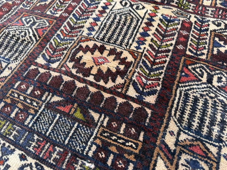 May include: A woven rug featuring a dense, repeating geometric pattern in shades of deep red, navy blue, cream, and accents of green. The design consists of interconnected rectangular panels, stylized floral motifs, and intricate borders.