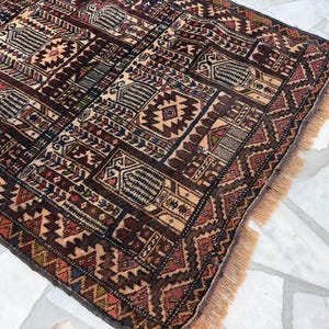May include: A rectangular area rug featuring a dense, repeating geometric pattern in shades of deep brown, rust red, cream, and navy blue. The rug has a woven texture with a short fringe along the edge and a complex grid of interconnected motifs.