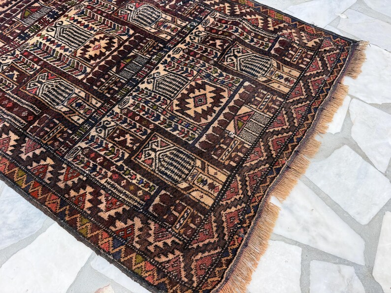 May include: A rectangular area rug featuring a dense, repeating geometric pattern in shades of deep brown, rust red, cream, and navy blue. The rug has a woven texture with a short fringe along the edge and a complex grid of interconnected motifs.