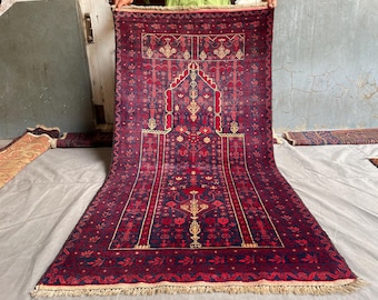 May include: A rectangular prayer rug featuring a deep purple and dark blue base with intricate red and cream floral and geometric patterns. The design includes a central mihrab arch motif, a decorative border, and fringed edges on both ends.