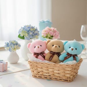 May include: Three plush teddy bears in pastel pink, tan, and light blue colours, each wearing a brown ribbon printed with the word Love, are nestled together inside a rectangular woven wicker basket lined with white lace fabric.