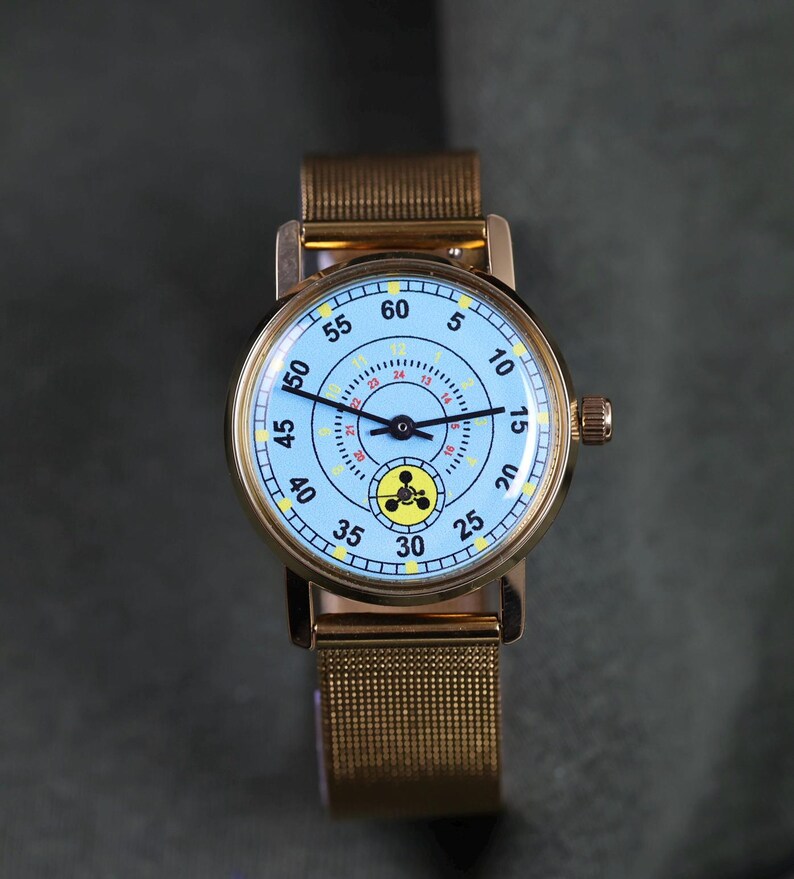 May include: A wristwatch with a gold-tone metal mesh band and a round gold-tone case. The light blue dial features black hour and minute hands, a black second hand, black numerals from 5 to 60, a 24-hour inner ring, and a yellow circular icon.