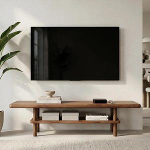 May include: A rectangular wooden media console with rounded edges and a lower shelf. The console features four cylindrical legs and holds two light-coloured storage boxes, a stack of books, a small bowl, a black electronic device, and a remote.
