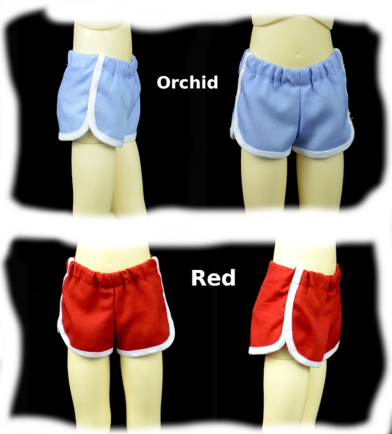 May include: Two pairs of doll shorts with white piping. The shorts on the top are orchid blue and the shorts on the bottom are red.
