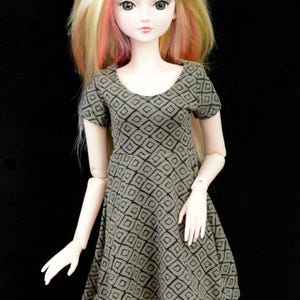 May include: A doll with blonde hair and pink highlights wearing a brown and black geometric print dress.