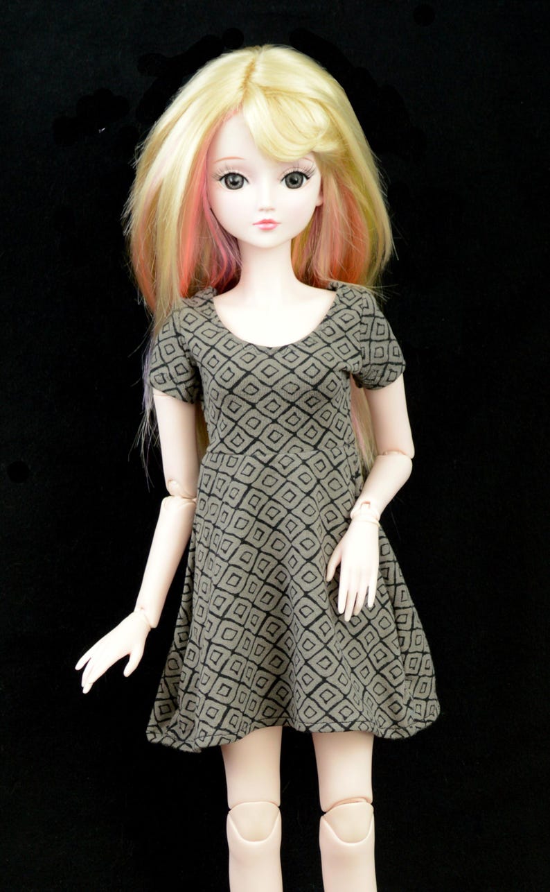 May include: A doll with blonde hair and pink highlights wearing a brown and black geometric print dress.