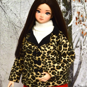 May include: A doll with long brown hair wearing a white turtleneck sweater, a leopard print jacket, and a red skirt. The doll is standing in front of a snowy background.