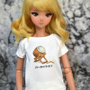 May include: A doll wearing a white t-shirt with a graphic of a Japanese drum and the text "パーカッション". The doll has long blonde hair and blue eyes.