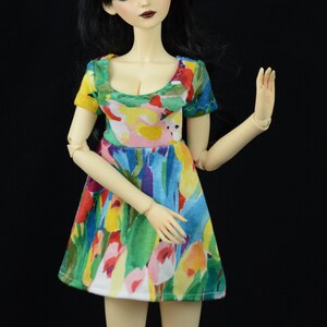 May include: A doll with black hair and a colorful floral dress. The doll has a white face with painted eyes and lips.
