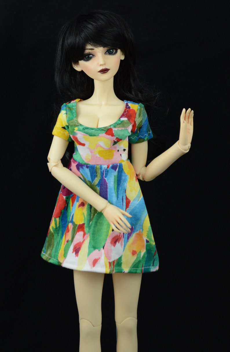 May include: A doll with black hair and a colorful floral dress. The doll has a white face with painted eyes and lips.