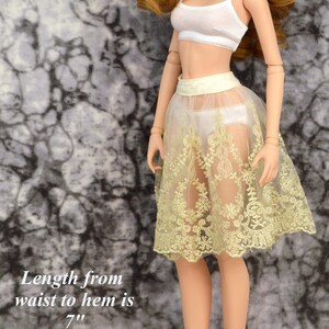 May include: A doll wearing a white crop top and a sheer yellow lace skirt with a satin waistband. The skirt is 7 inches long and the waistband adjusts from 6.25 to 7.25 inches.