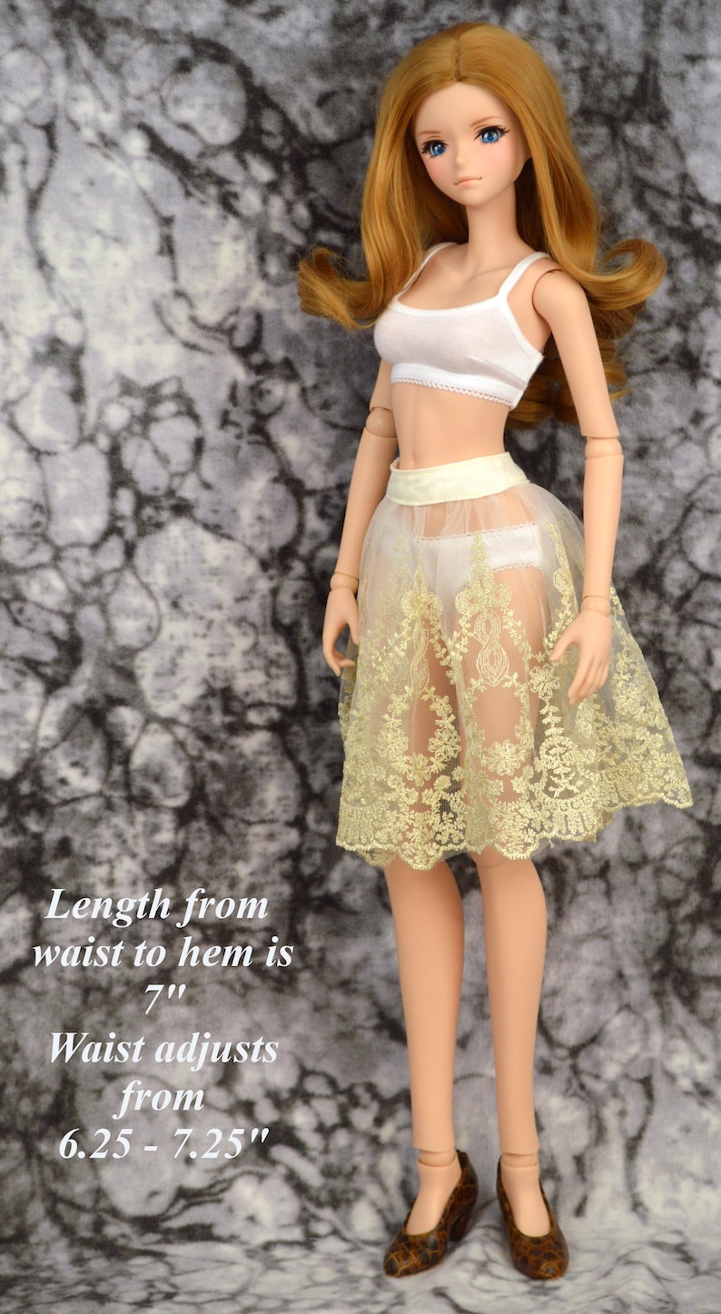 May include: A doll wearing a white crop top and a sheer yellow lace skirt with a satin waistband. The skirt is 7 inches long and the waistband adjusts from 6.25 to 7.25 inches.