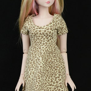 May include: A doll with blonde hair and pink highlights wearing a brown and tan leopard print dress.