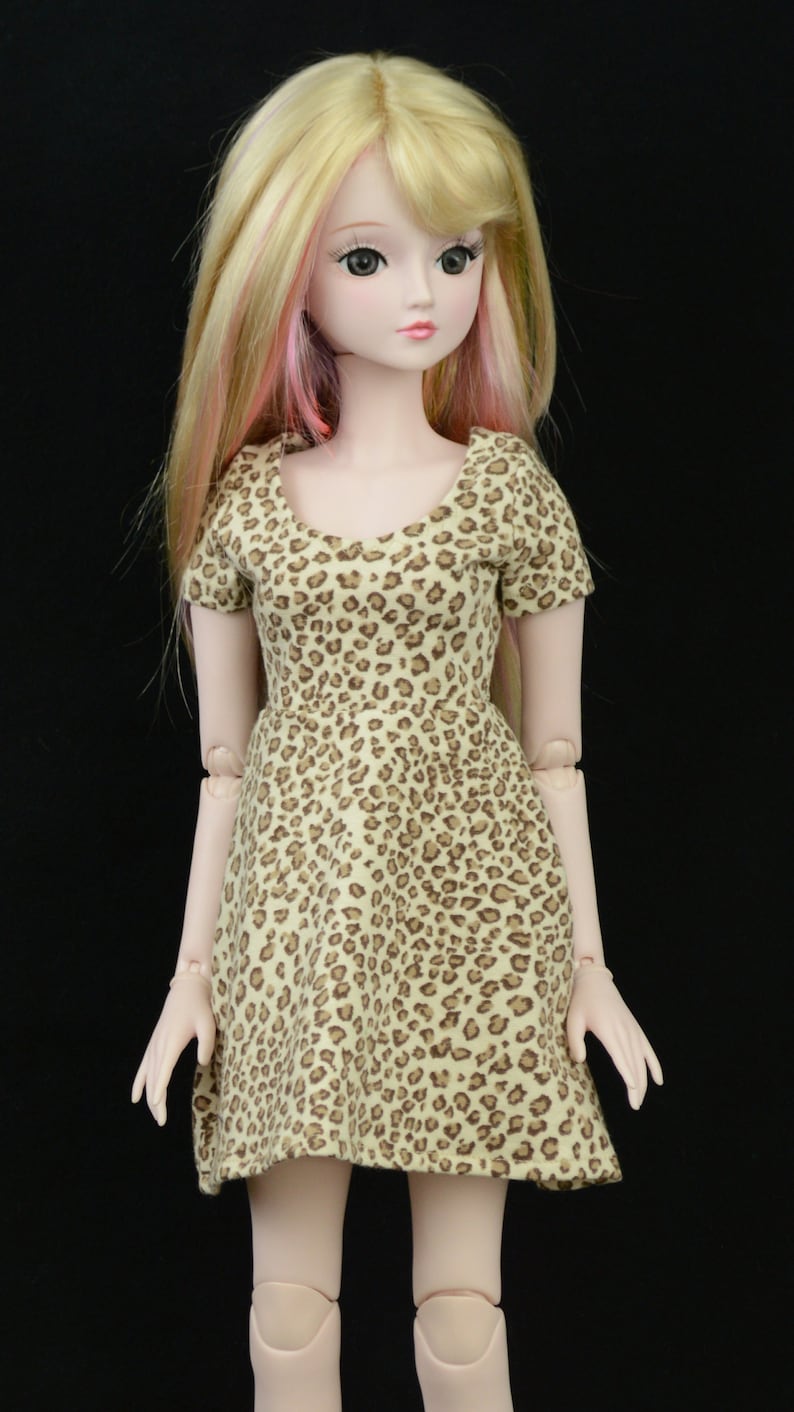 May include: A doll with blonde hair and pink highlights wearing a brown and tan leopard print dress.