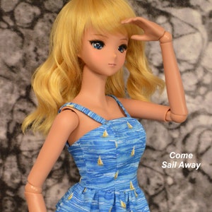 May include: A doll with long blonde hair wearing a blue and white top with a sailboat pattern. The top has a ruffled hem and the text "Come Sail Away" is visible in the image.