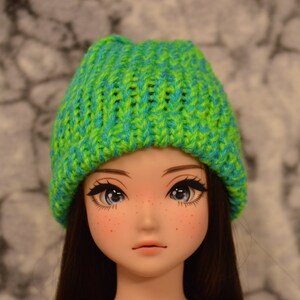 May include: A green and blue striped knit beanie hat. The hat is made of soft yarn and has a ribbed texture.