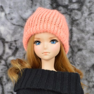 May include: A doll with long blonde hair wearing a pink knitted beanie and a black sweater.