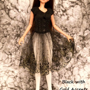 May include: A black doll with long brown hair wearing a black knitted top and a black tulle skirt with gold accents.