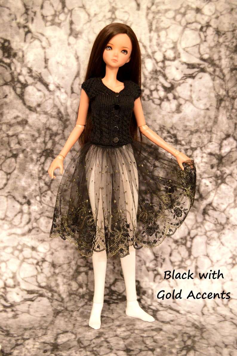 May include: A black doll with long brown hair wearing a black knitted top and a black tulle skirt with gold accents.