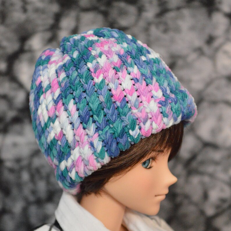 May include: A colourful knitted hat with a pink, blue and green colour scheme. The hat is made of a soft, textured yarn and has a slouchy fit.