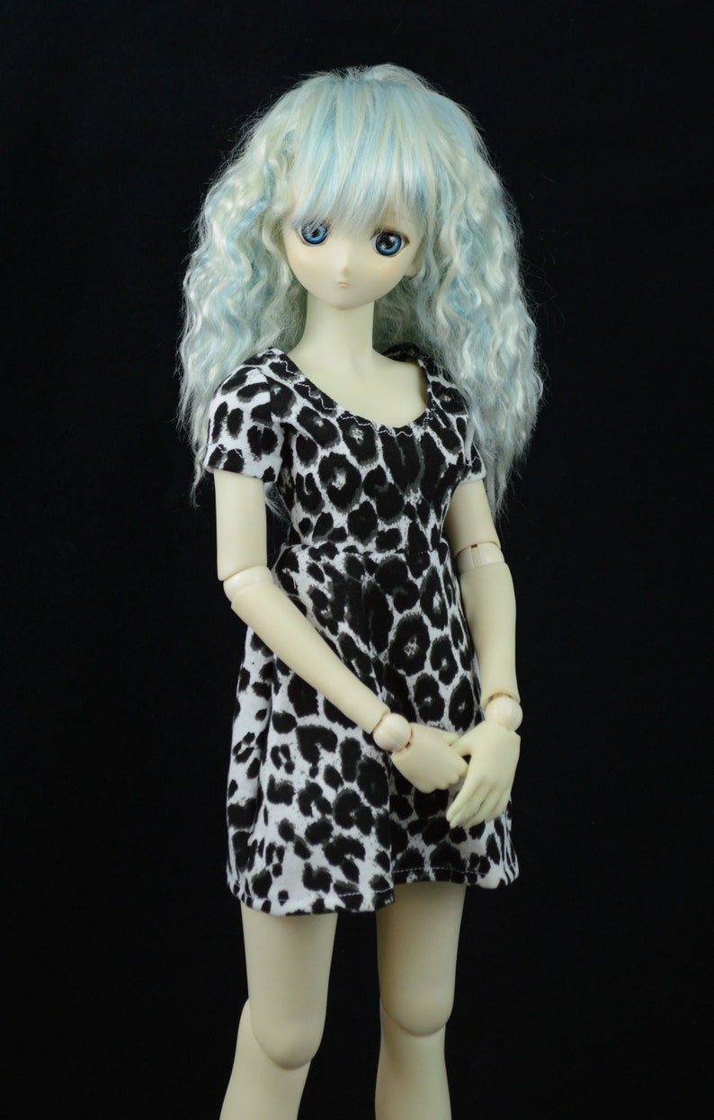 May include: A doll with light blue curly hair wearing a black and white animal print dress.