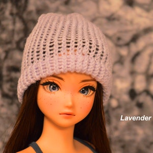May include: A doll with long brown hair wearing a lavender knitted beanie. The doll has blue eyes and freckles.