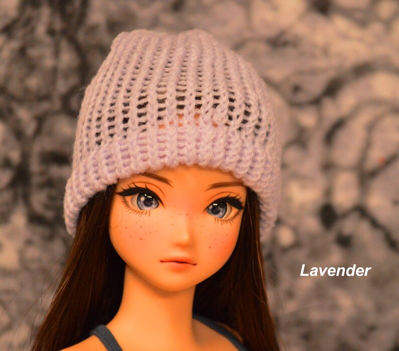 May include: A doll with long brown hair wearing a lavender knitted beanie. The doll has blue eyes and freckles.