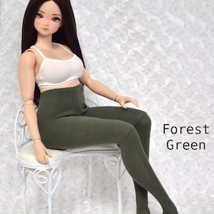 May include: A doll wearing a white crop top and forest green leggings. The doll is seated on a white chair with a decorative design. The text "Forest Green" is visible in the image.