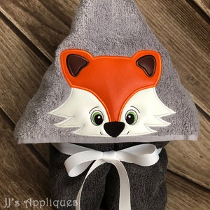 May include: A gray hooded towel with a fox face embroidered on the hood. The fox has orange fur, white accents, and green eyes. The towel has a white ribbon tied around it.