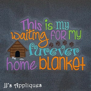 May include: A purple, orange, and green embroidered design on a gray fabric background. The design says "This is my waiting for my forever home blanket". There is a brown dog house with a bone and a bowl in front of it. There are also four paw prints above the word "forever".