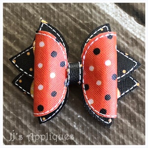 Op de afbeelding: Een zwarte en oranje gepolka-dotte strik met een zwarte en witte gestikte rand. De strik heeft een zwart midden en is gemaakt van stof.