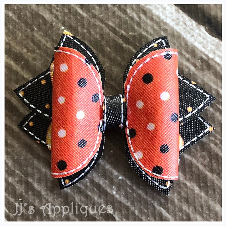 Op de afbeelding: Een zwarte en oranje gepolka-dotte strik met een zwarte en witte gestikte rand. De strik heeft een zwart midden en is gemaakt van stof.