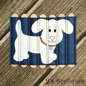 May include: A white dog applique with a brown collar and silver tag, stitched onto vertical strips of dark blue material. The strips are attached to light-colored wooden craft sticks at the top and bottom. The text JJ's Appliques is visible.