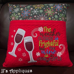 May include: A decorative pillow with a red front featuring embroidered wine glasses and the phrase "The weather outside is frightful but the wine is so delightful." The top section is patterned with snowflakes and candy canes.