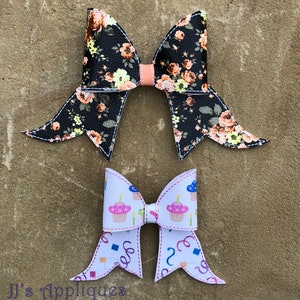 May include: Two decorative hair bows. The top bow features a black background with a floral pattern in shades of peach, yellow, and white. The bottom bow has a white background with cupcake and confetti designs. The bows are stitched with white thread.