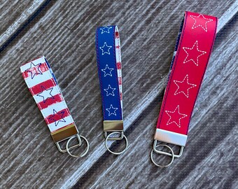 May include: Three keychains with red, white, and blue star designs. The keychains are made of fabric and have a silver metal ring.